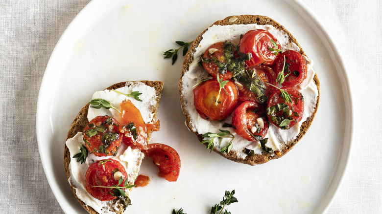An open-faced tomato sandwich on a seeded bagel with herbs