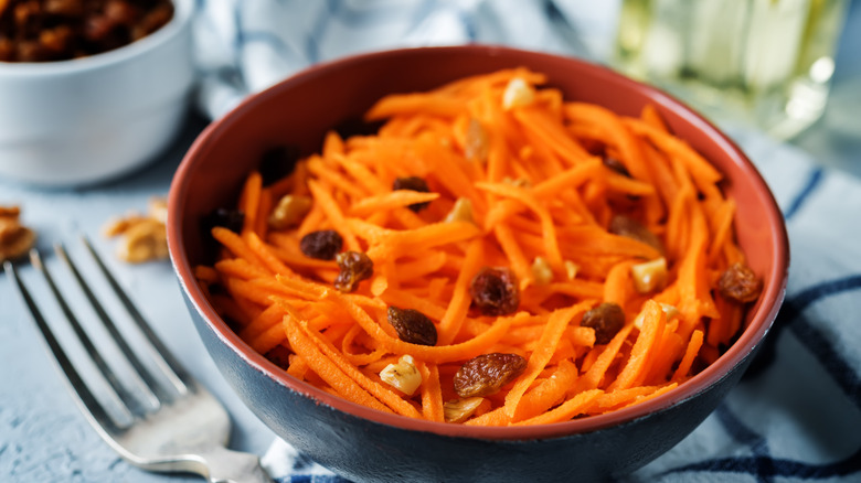 A close-up of carrot-raisin salad in a bowl, next to a fork