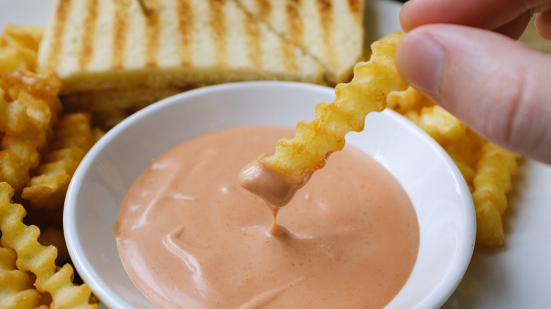 hand dipping crinkle-cut fries into fry sauce.