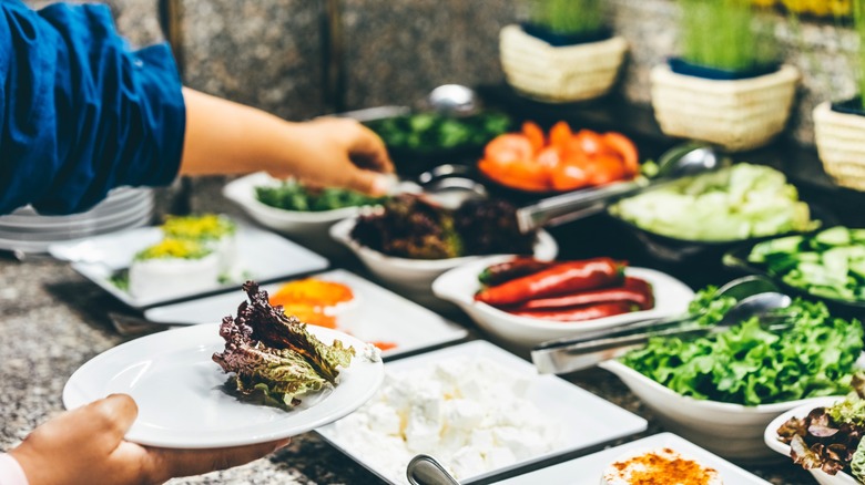 Someone adding vegetables to their plates at a salad bar