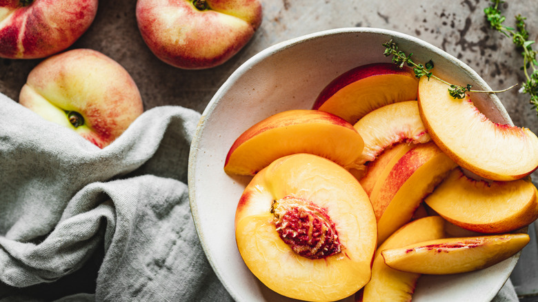 Sliced peaches in a bowl next to fresh peaches on a counter