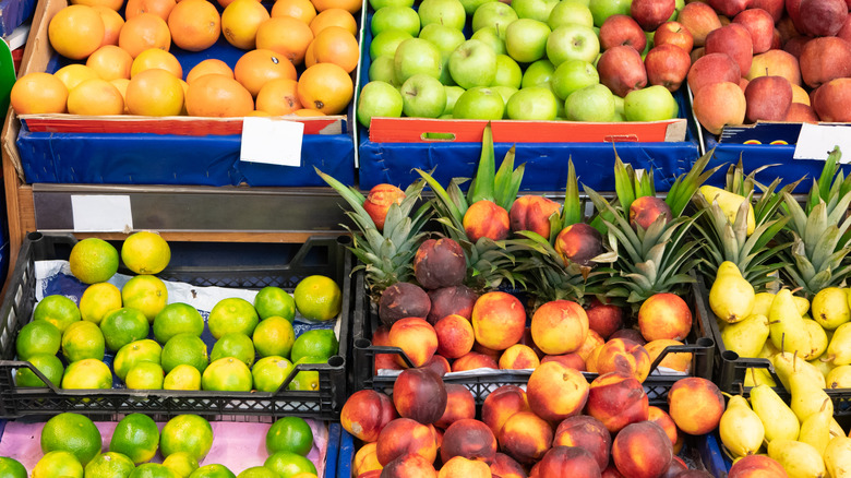 A fruit display in a grocery store with cases of oranges, apples, peaches, pineapples, pears, and limes