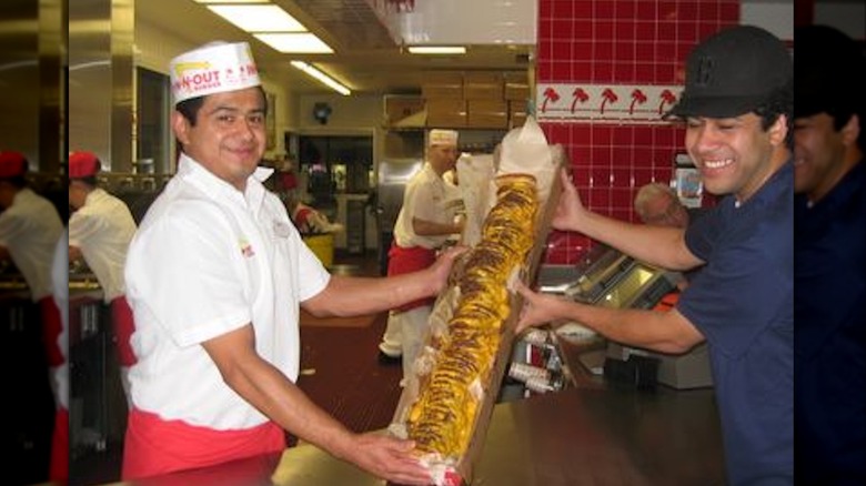 Employees at an In-N-Out Burger holding 100x100 burger in a long cardboard box