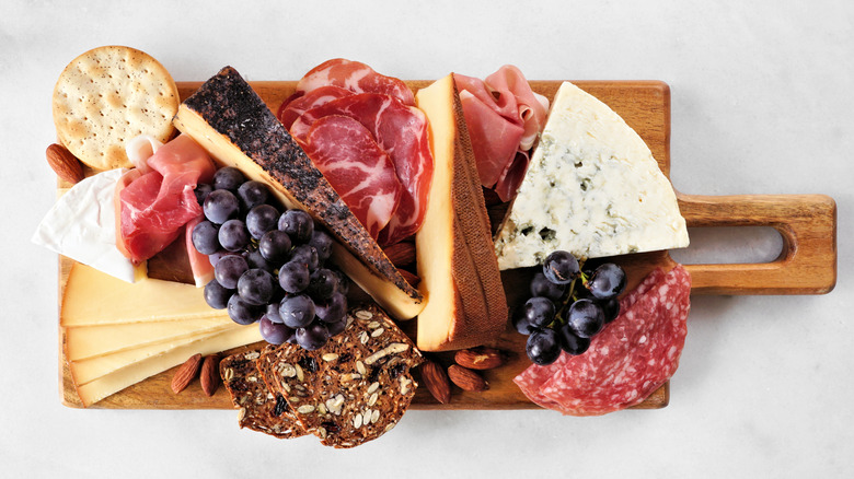 Wooden charcuterie board with wedges of cheese, crackers, grapes, and cured meats