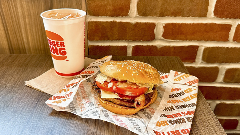 A ﻿Peppercorn BLT Whopper sits on a wooden table on its wrapper next to a Burger King cup