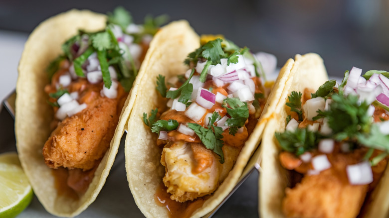 A close up of three crispy fish tacos topped with bright pieces of onion and coriander
