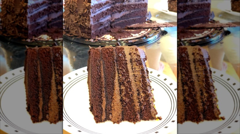 A slice of Costco's four-layer chocolate cake on a plate with the cake in the background
