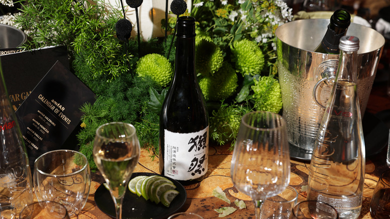 A bottle of Sake on a table with wine glasses and an ice bucket holding another sake bottle