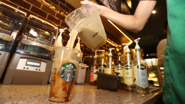 A Starbucks barista pouring a drink into a cup lined with caramel sauce
