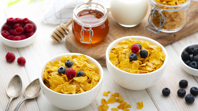 Bowls of cereal topped with fruit and surrounded by jars of honey, spoons, and more bowls of fruit