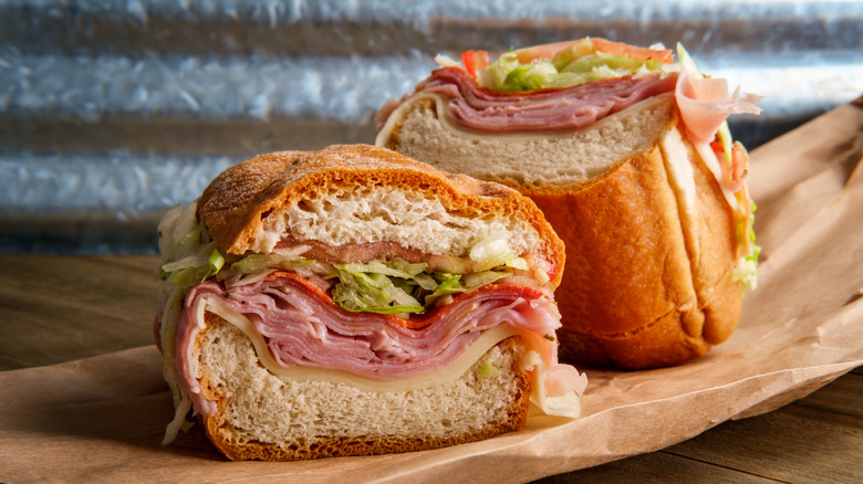 An Italian sub sandwich that has been sliced in half with meats and cheeses on brown paper bag