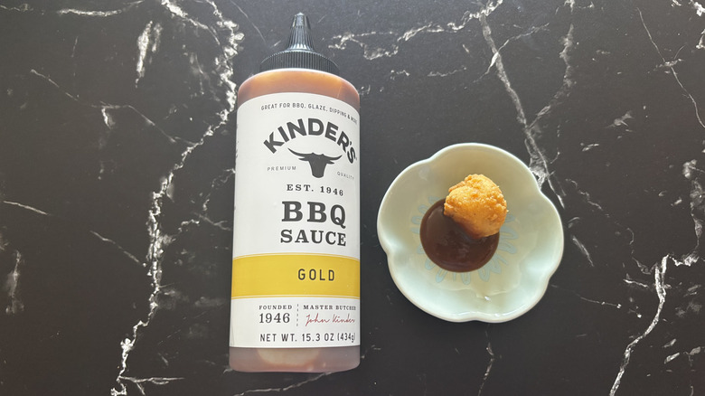 A bottle of Kinder's Gold BBQ sauce next to a bowl of sauce and a chicken nugget