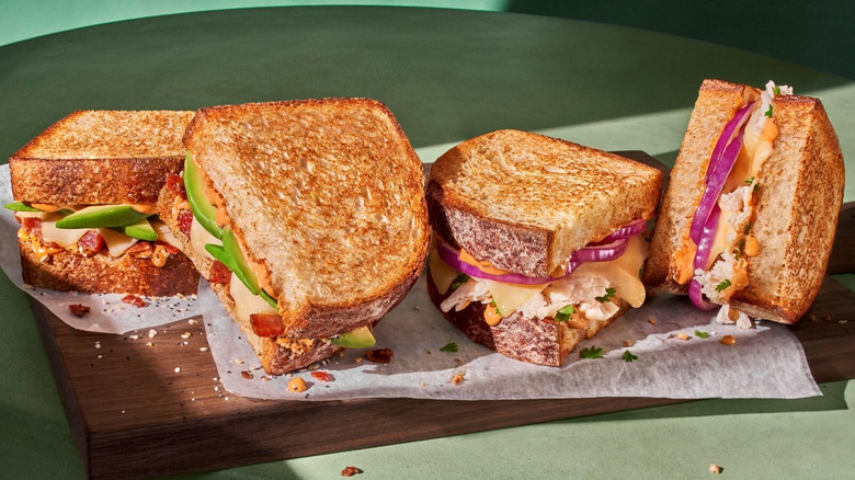 Grilled sourdough sandwiches on a wooden table with paper underneath them