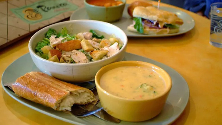 A bowl of soup, a salad and a sandwich on a blue plate on a Panera restaurant table