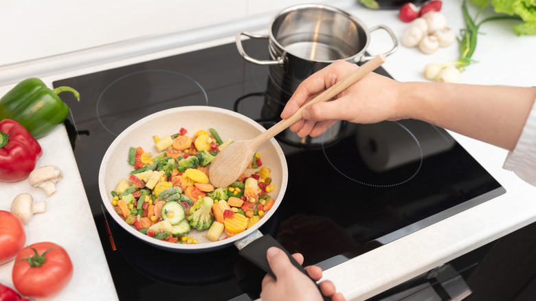 A person using an induction stovetop to cook vegetables in a pan