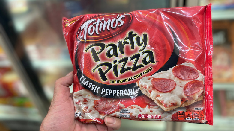A hand holding Totino's Pizza Party package in front of a store freezer