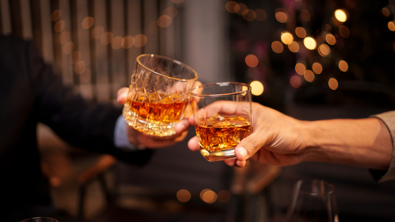 Two people toasting with glasses of bourbon
