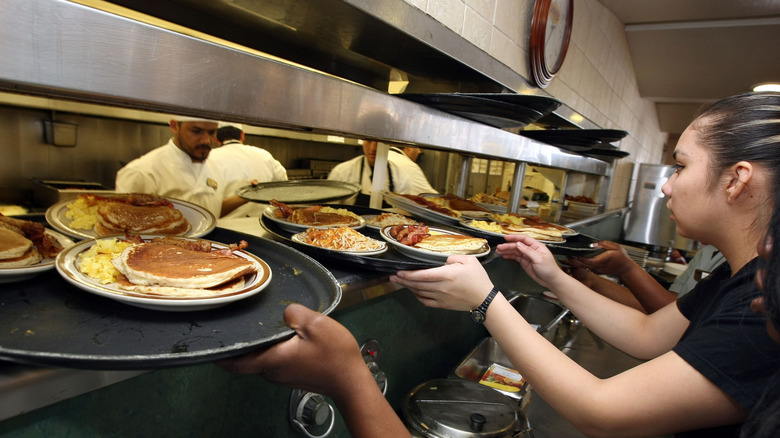 Servers grabbing trays of food from the kitchen at Denny's