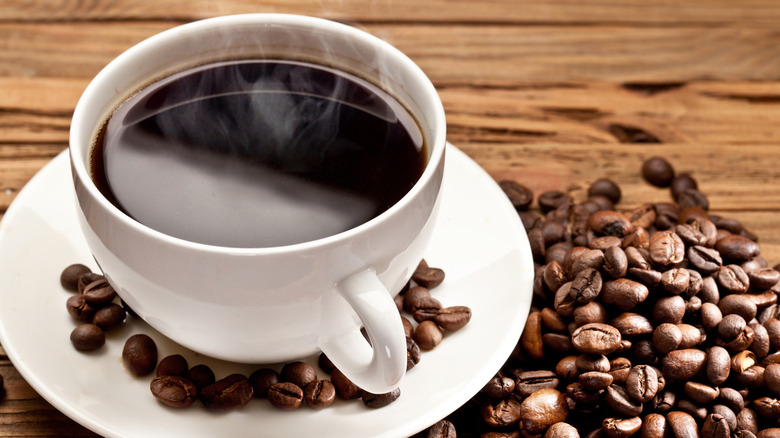 a cup of black coffee sits on a saucer next to a pile of coffee beans.