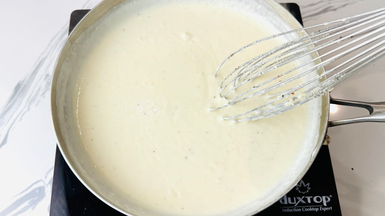 Alfredo sauce with whisk in pan