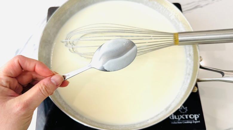 Hand holding spoon over pan with white sauce
