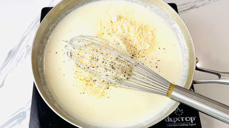 Alfredo sauce with seasonings, cheese, and whisk in pan