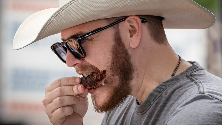Man in cowboy hat and sunglasses, eating a rib