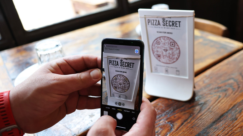Person holding phone up to scan a QR code menu at a pizza place