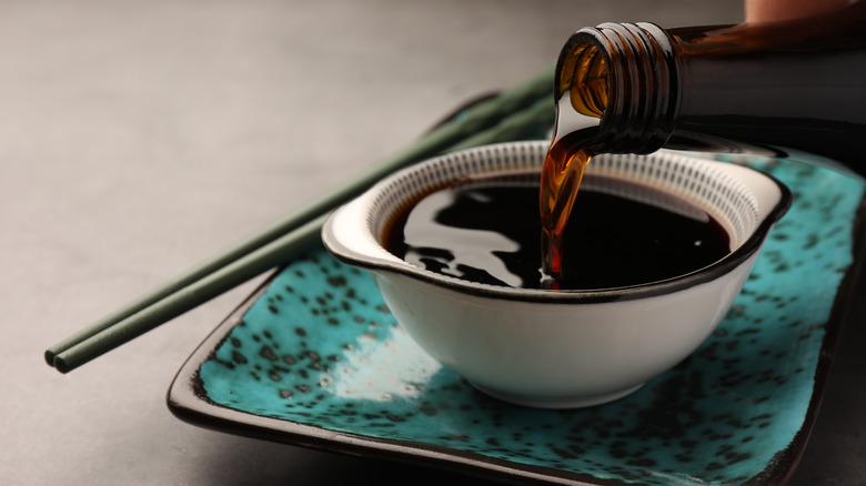 Soy sauce being poured into a white bowl on top of a turqoise plate