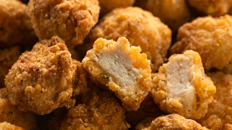 a close-up view of pieces of popcorn chicken, one of which is sliced in half to show the interior