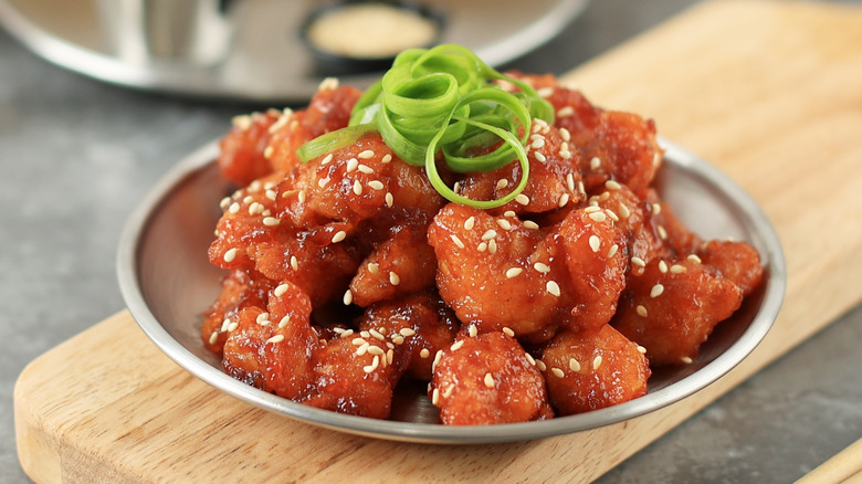 a small plate of sauce-coated popcorn chicken garnished with sesame seeds and scallions