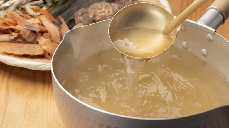 a gold ladle scooping some stock in a pot with a plate of stock ingredients behind it.