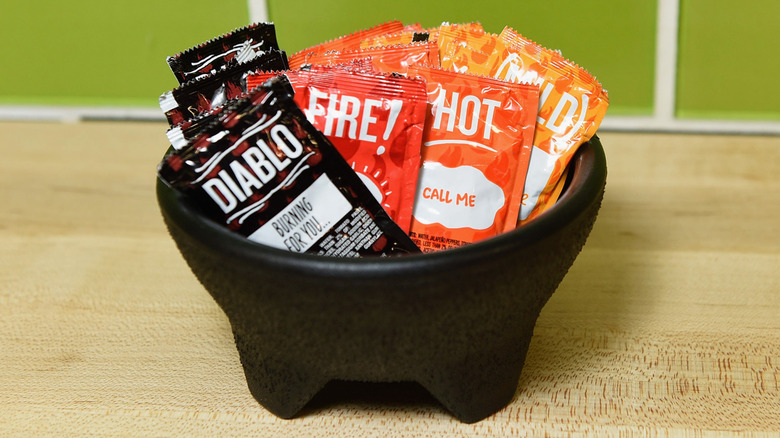 Packages of Taco Bell sauces including Mild, Hot, and Diablo in a black bowl on a wooden table