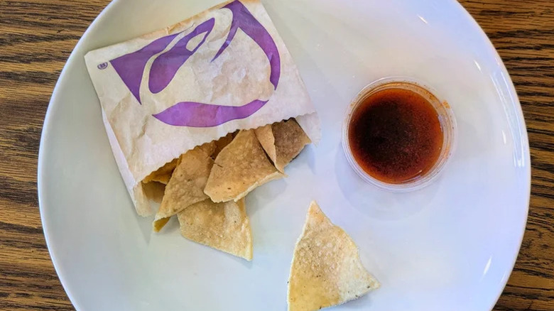A plate with some Taco Bell tortilla chips and a small plastic container of red sauce
