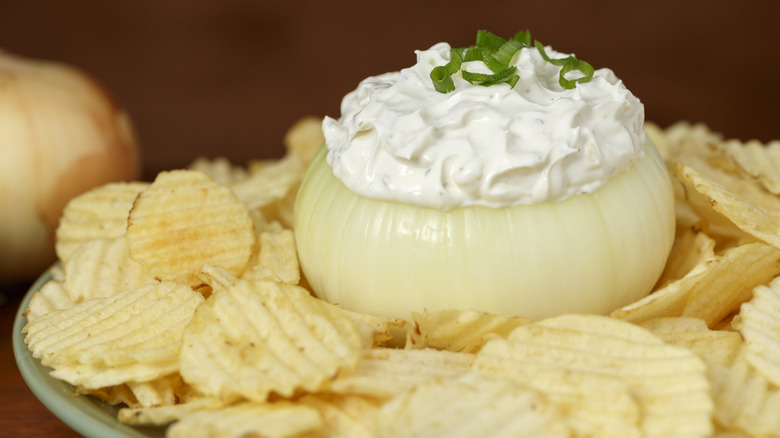 Onion dip served out of a hollow onion in the center of a platter with ruffled potato chips spread around it