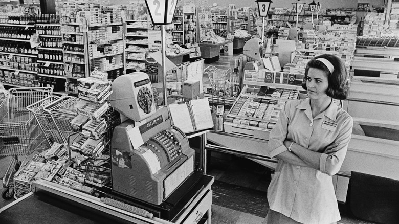 an employee stands at a checkout lane in supermarket in the 1960s