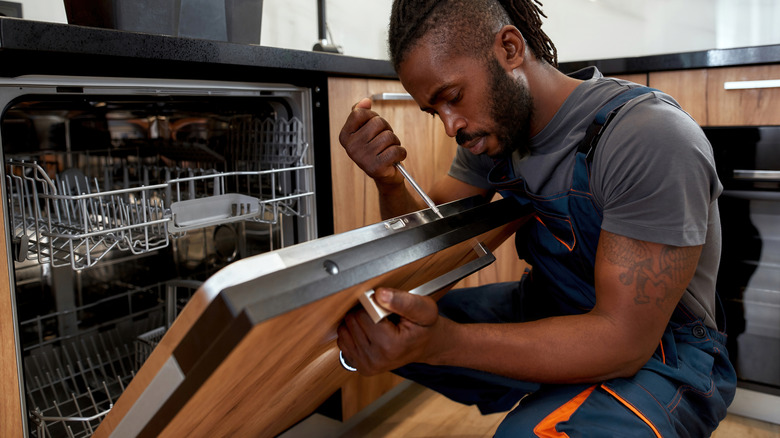 man with screwdriver installing dishwasher with matching panel to rest of cabinets