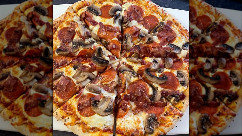 Homemade pizza sliced and topped with pepperoni, mushrooms, and bacon strips