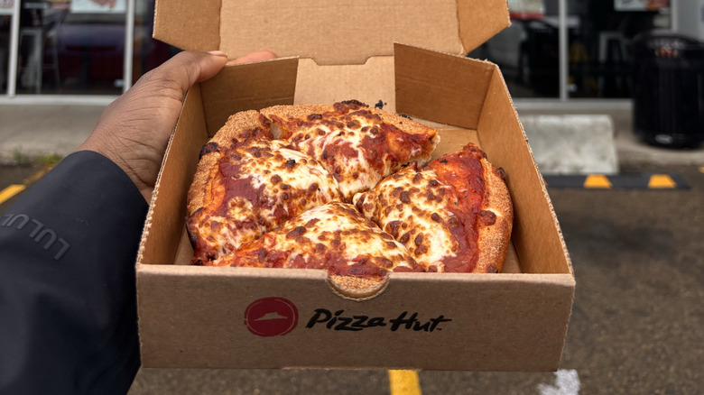 Hand holding a box of Pizza Hut personal pie in parking lot