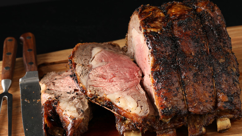 Cut prime rib roast on wooden board with cutting knives