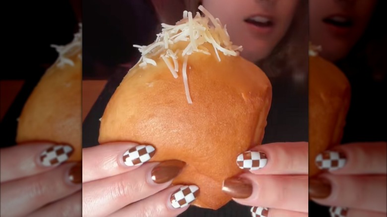TikToker holding Texas Roadhouse roll with garlic butter and Parmesan cheese