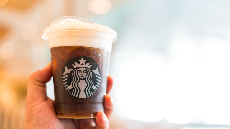 Someone holds up a Starbucks coffee with cold foam