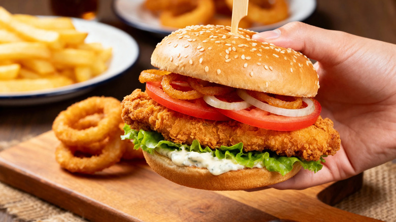 A fried chicken sandwich with lettuce tomatoes onions and crispy onions
