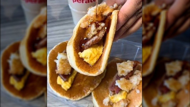 Syrup being poured onto a folded over pancake containing sausage and eggs