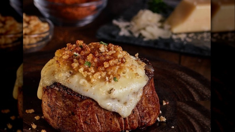 A LongHorn Steakhouse filet covered in its parmesan crust on a dark background with parmesan and spices visible