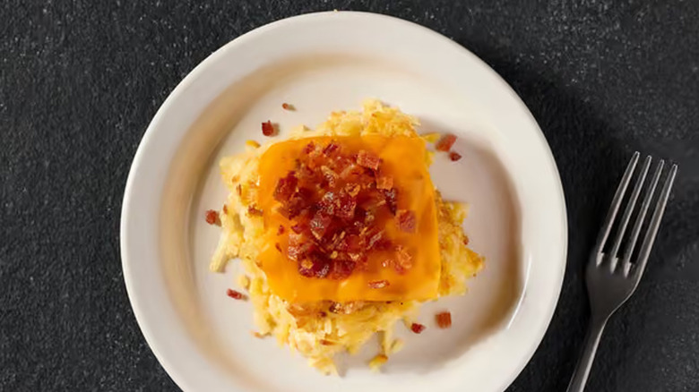 A plate of the loaded hash brown casserole sitting in a white dish on a blue and white background with a fork beside it