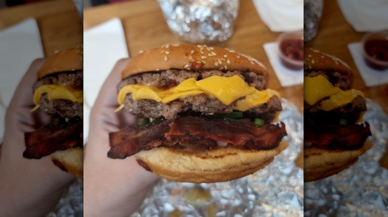 A bacon cheeseburger from Five Guys with melty cheese between two patties and a large pile of crispy bacon visible under the patties.