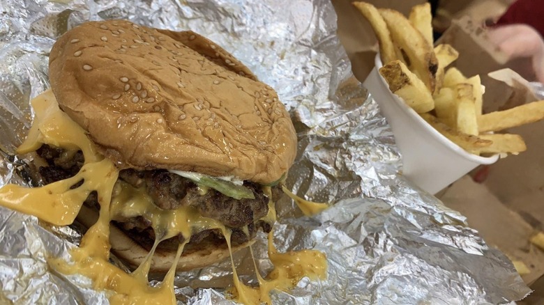 A Five Guys cheeseburger with melted cheese on the sides onto the foil wrapper.