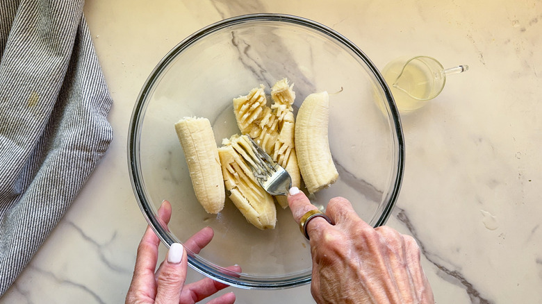 fork mashing bananas in glass bowl
