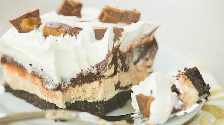 A layered slice of peanut butter pudding pie with a piece taken out by a fork